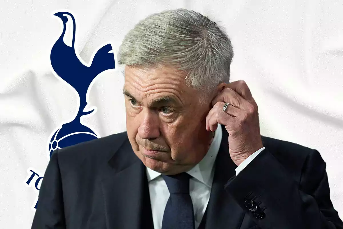 Carlo Ancelotti in a dark suit touches his ear in front of the Tottenham Hotspur logo.