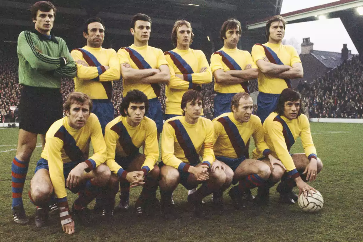 A football team posing on the field in yellow uniforms with blue and red diagonal stripes.