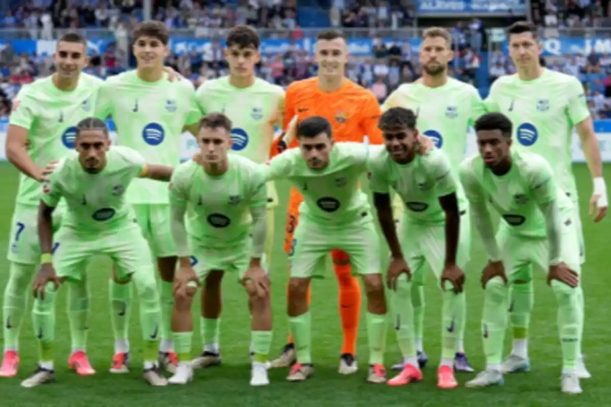 A football team posing on the field before a match, wearing light green uniforms and a goalkeeper in an orange uniform.