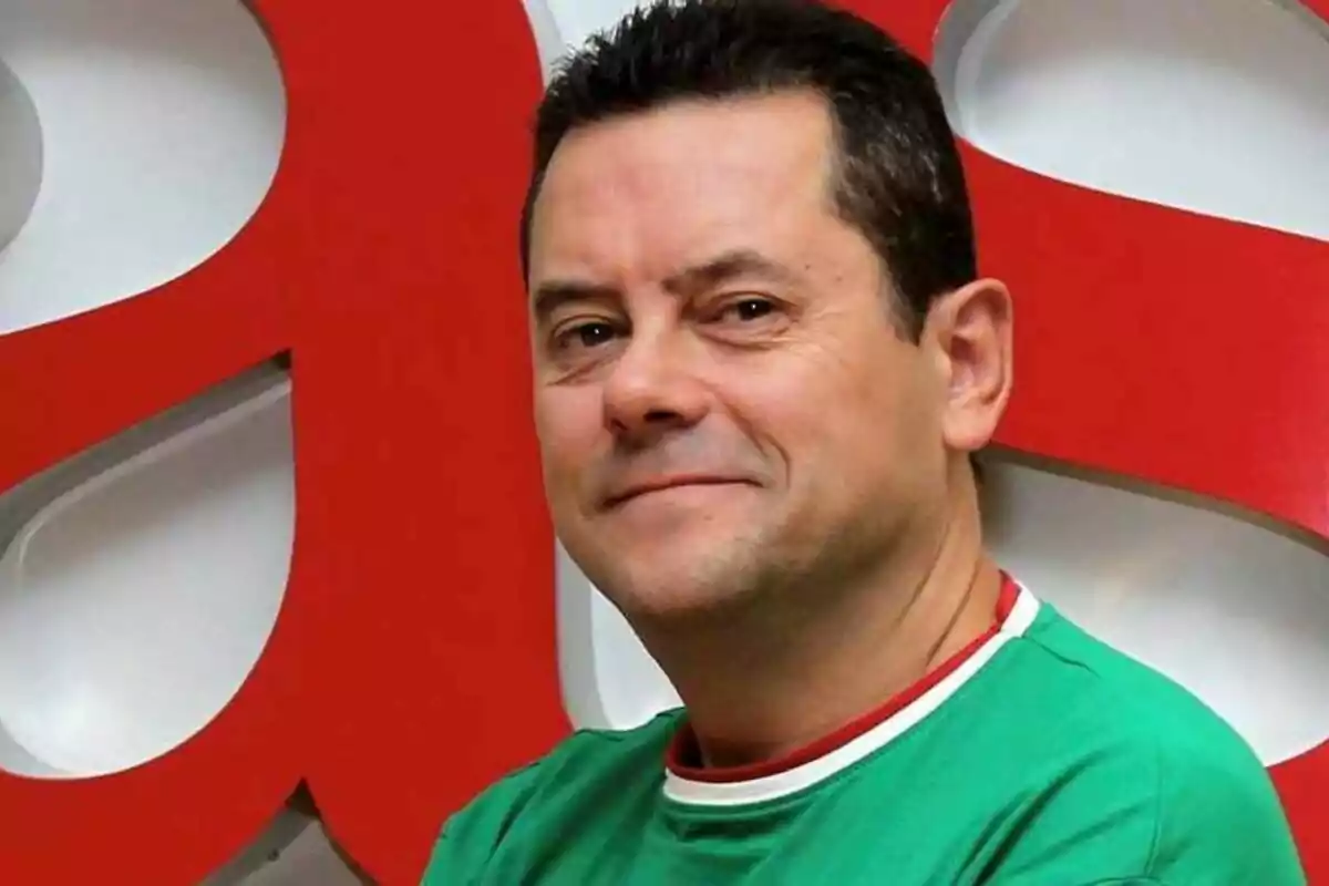 Man in green t-shirt smiling in front of a red and white background.