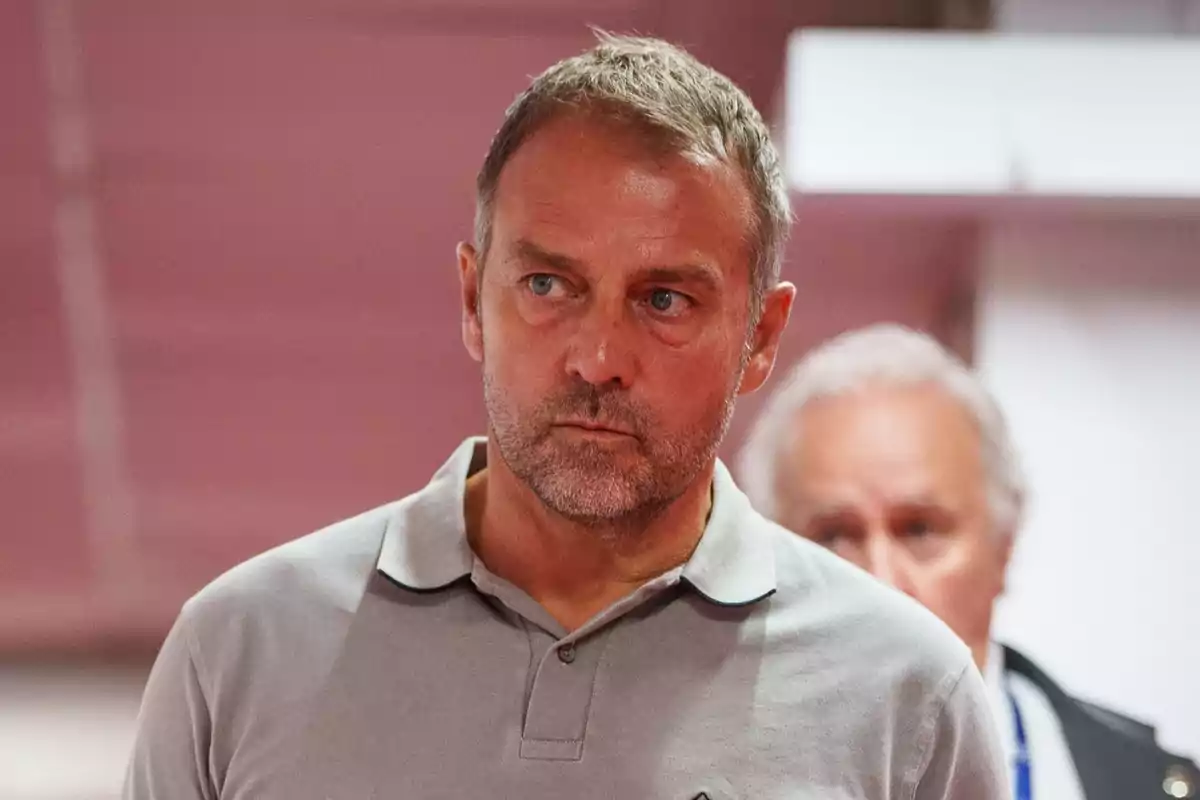 A man with a serious expression and a short beard, dressed in a grey polo shirt, with an out-of-focus background.