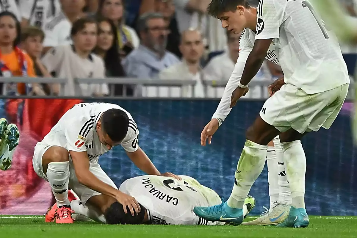 Football players on the field, one of them on the ground while his teammates assist him.