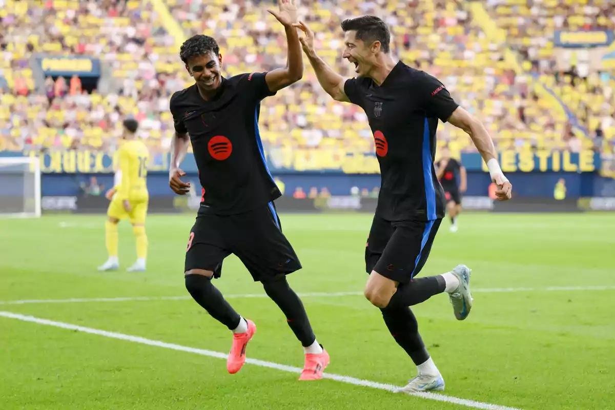 Two soccer players celebrate a goal with a handshake in a stadium full of spectators.