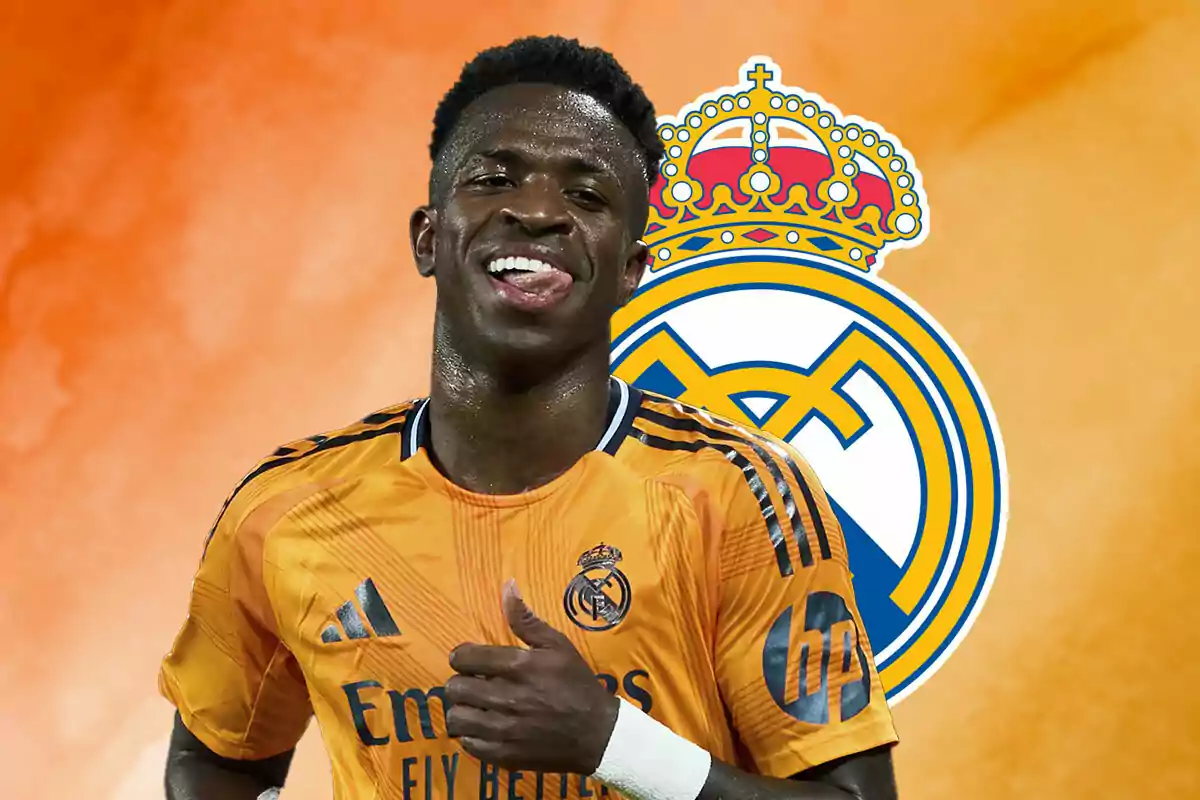 Vinicius in an orange uniform smiles in front of the Real Madrid crest on an orange background.